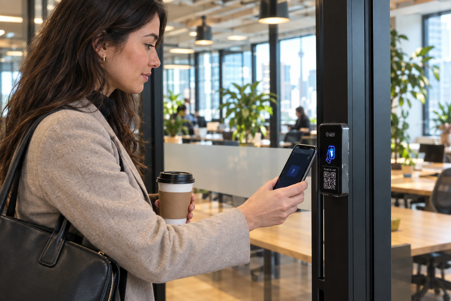 A woman with a coffee taps her phone on the reader at the glass door of an open-plan office.